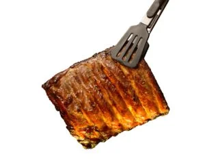 A tong holding a juicy piece of grilled pork ribs, showcasing its texture and color against a white background.